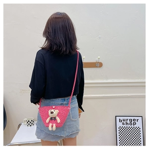Rear view of a pink woven mini bag with a plush bear charm worn by a model