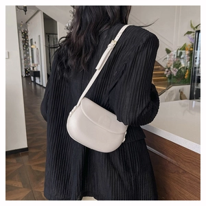 Detailed view of the cream-colored saddle bag worn over a black pleated blazer