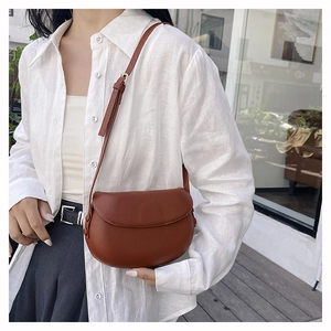 Brown leather saddle bag with adjustable shoulder strap worn by model in white shirt