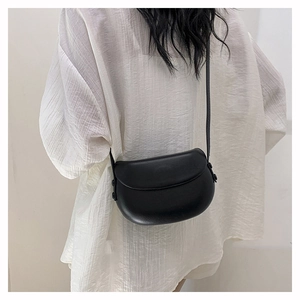 Detail view of a black matte leather saddle bag worn as a crossbody on a casual outfit