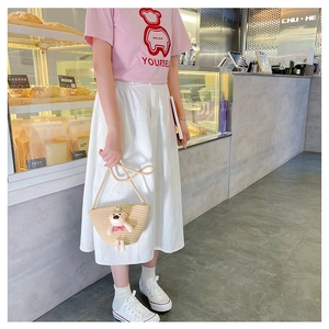 Straw mini crossbody bag with cute plush bear charm styled in a cozy cafe setting