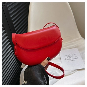 Close-up of red leather saddle bag with flap closure and adjustable strap on a chair