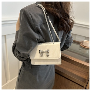 Detail of white crossbody bag featuring a silver butterfly clasp and chain strap