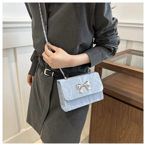 Detail of light blue pleated cloud bag featuring a silver metal bow and chain strap