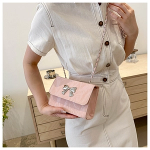 Chic pink square chain bag with silver bow accent worn by model in a home setting