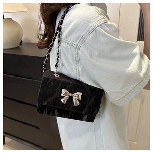 Detail of black pleated crossbody bag with silver bow and woven chain strap on shoulder