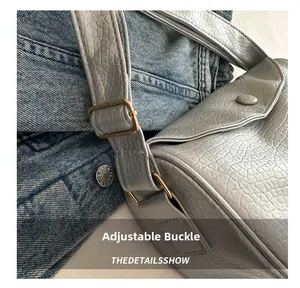 Detail of adjustable strap with bronze buckle on silver-grey textured dumpling bag