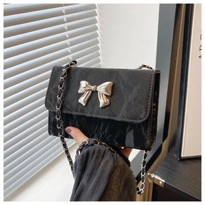 Detail of black crossbody bag featuring pleated texture and silver metal bow buckle