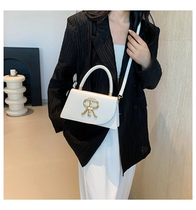 Detail of white leather shoulder bag with gold metal logo on a model in a black blazer