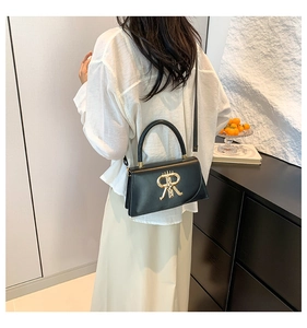 Detail of elegant black crossbody bag with gold R-logo buckle shown on a model
