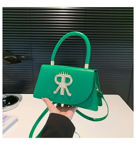 Détail du sac à main vert vif avec fermoir doré en forme de R et poignée rigide
