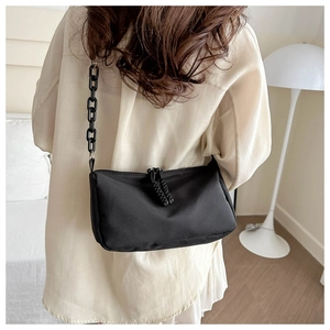 Detail of black nylon crossbody bag featuring chunky resin chain and woven zipper pulls