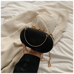 Detailed view of a black sequin oval clutch with gold bow clasp and metallic chain strap