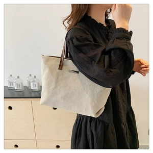 Detail of a large beige canvas tote bag with brown straps in a lifestyle setting