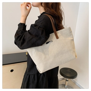 Detail of large canvas tote bag with brown leather handles and silver metal plaque