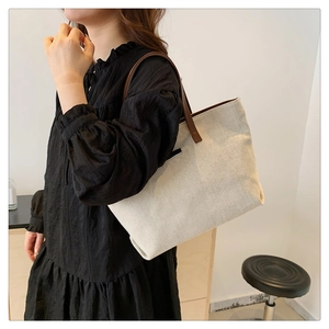Detail of minimalist canvas tote bag with brown leather straps worn by a model