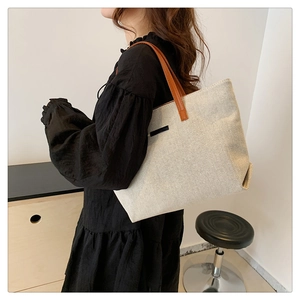 Detail of canvas tote bag with brown leather handles and side tag on a shoulder