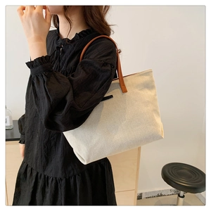 Detailed view of cream canvas tote bag with brown straps worn by a model in a room