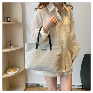Minimalist beige canvas tote bag with black leather straps shown in a lifestyle setting