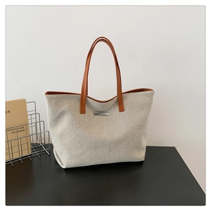 Close-up of cream white canvas tote bag with brown leather handles on dark desk