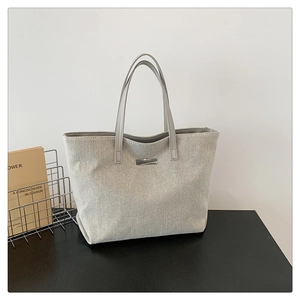 Close-up of canvas tote bag with leather handles and silver metal logo on front