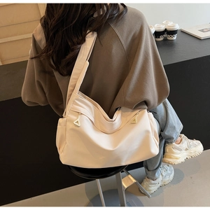 Detail of cream nylon tote bag featuring a wide shoulder strap and metal zip puller