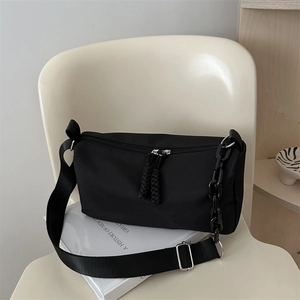 Minimalist black nylon crossbody pillow bag with wide strap and chain on a chair