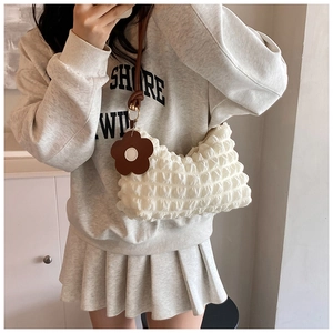 Detail of white bubble texture fabric on shoulder bag with brown flower charm accent