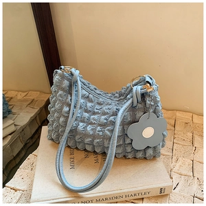 Detail of light blue bubble textured handbag with leather flower charm on cream books