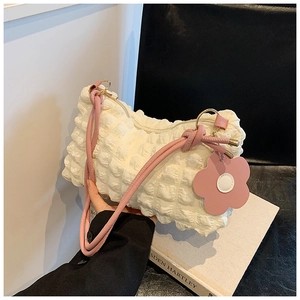 Close-up of beige pleated shoulder bag with pink floral charm and waffle texture fabric