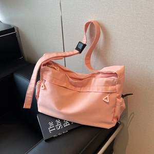 Pink waterproof nylon tote bag with adjustable black strap on black leather sofa
