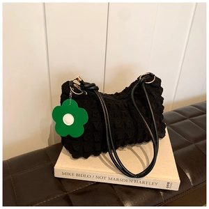 Detail of black bubble textured shoulder bag with floral charm on a white book