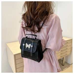 Rear view of model wearing a black fashion backpack with silver butterfly detail