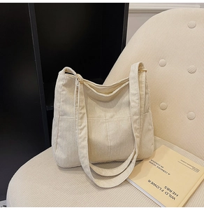 Close-up of beige corduroy shoulder bag with ribbed texture on a soft fabric chair