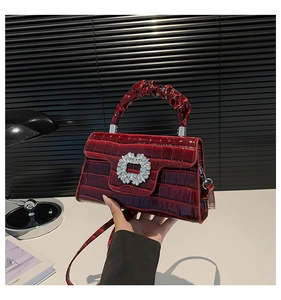 Detail of burgundy crocodile-embossed handbag with sparkling rhinestone clasp and ruched handle