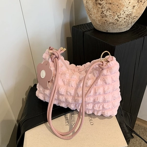 Pink bubble texture shoulder bag with floral charm displayed on minimalist white books