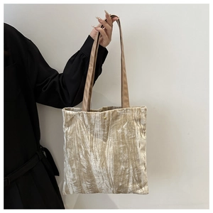 Detail of pleated champagne velvet tote bag featuring a metallic snap and brown PU straps
