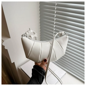 Detail of white leather croissant bag featuring pleated texture and woven knot handle design