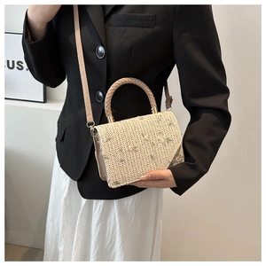 Dettaglio borsa a tracolla intrecciata beige con ricamo floreale e manico circolare