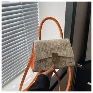 Détail du sac bandoulière en paille avec broderie florale et poignée en cuir orange