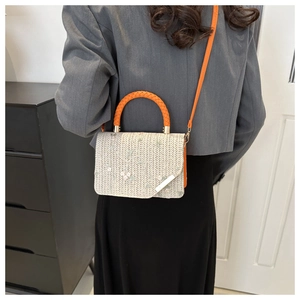 Dettaglio del ricamo floreale su borsa tessuta beige con manico arancione acceso
