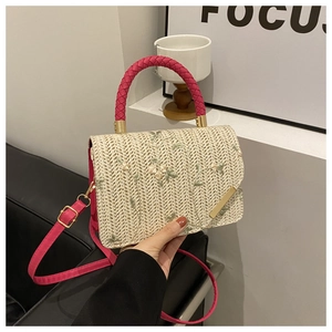 Dettaglio ricamo floreale su borsa in paglia beige con manico rosa e chiusura dorata