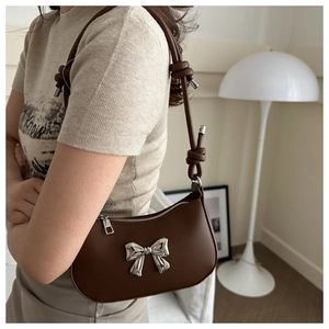 Detail of a brown leather shoulder bag with silver metal bow and knotted strap