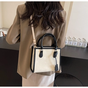 Détail d'un sac cabas crème avec bordure noire porté sur un blazer marron élégant