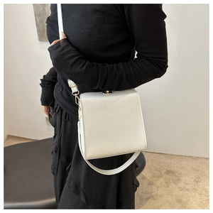 Détail d'un sac boîte carré blanc minimaliste avec serrure dorée sur tenue noire