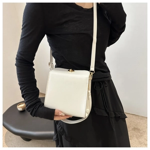 Gros plan d'un sac carré blanc en cuir avec fermoir doré porté sur une tenue noire