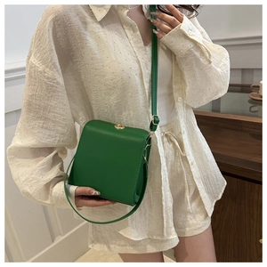 Gros plan d'un sac bandoulière vert en cuir avec fermoir doré porté par un mannequin