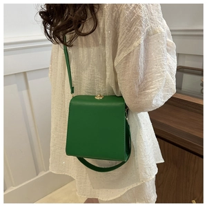 Gros plan d'un sac à bandoulière carré en cuir vert avec fermoir tournant en métal doré