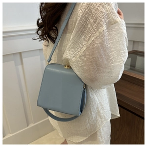 Vue latérale d'un mannequin portant un sac bandoulière en cuir bleu clair à fermoir doré