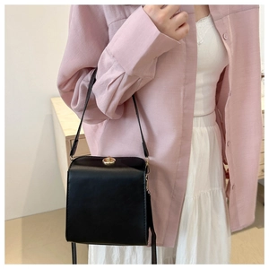 Détail d'un sac à bandoulière carré noir avec fermoir doré porté par un mannequin